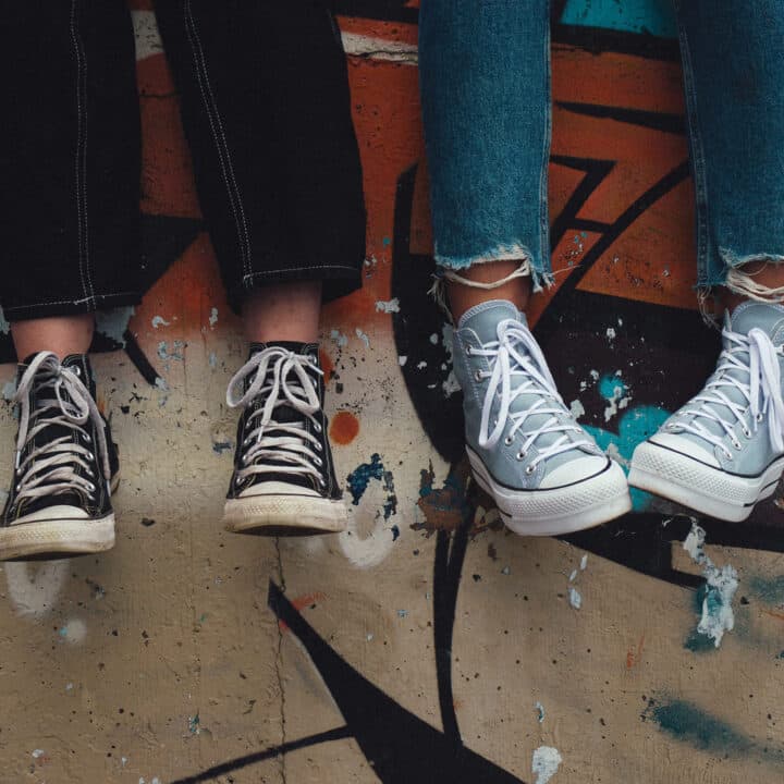 Zwei Personen sitzen auf einer Graffiti Wand und sie tragen dieselben Schuhe