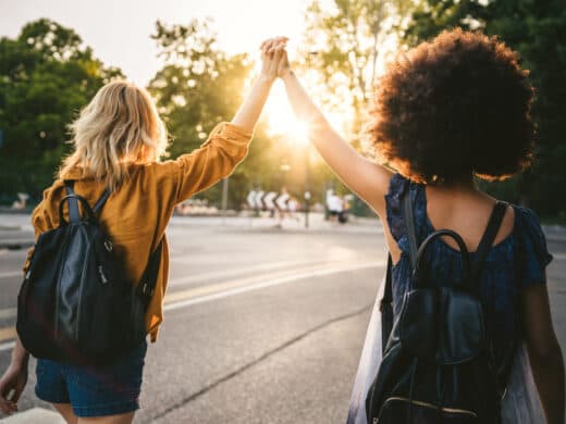 Zwei junge Frauen strecken gemeinsam ihr Hände in die Luft und laufen Richtung Sonnenuntergang